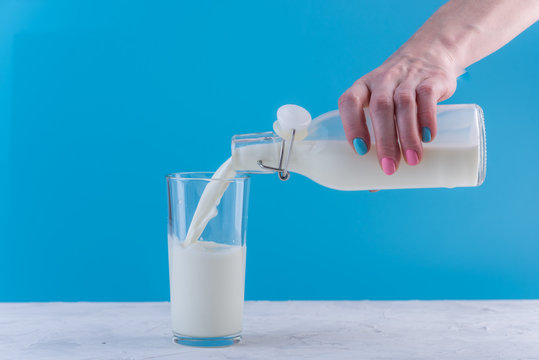 Woman's hand pours fresh milk from a bottle into a glass on a blue background. Healthy dairy products with calcium