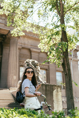 beautiful smiling girl in sunglasses standing with bicycle and using smartphone