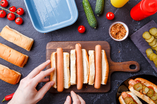 Image from above of man doing hotdogs on cutting board on table with sausages