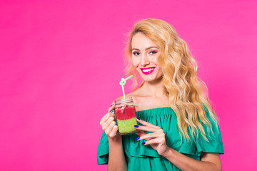 Young beautiful woman with green smoothie on pink background with copyspace
