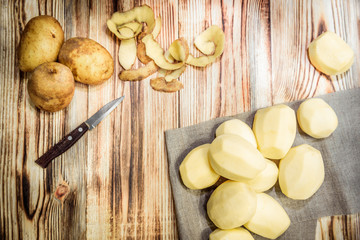 Raw peeled sliced potato, pile of potatoes and knife on rustic wooden table.