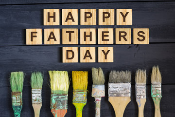 Happy Father's Day inscription on wooden cubes with different paint brushes on a wooden background....