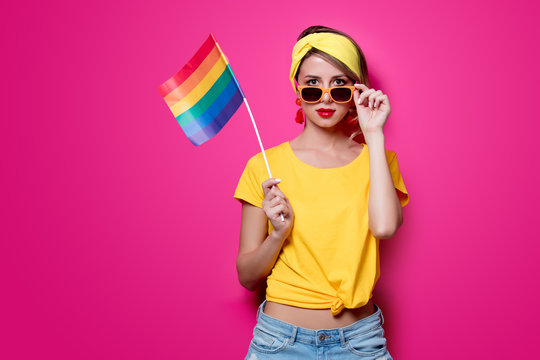 Young girl in yellow t-shirt and blue jeans holding big LGBT flag on pink background
