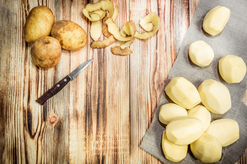 Raw peeled sliced potato, pile of potatoes and knife on rustic wooden table.