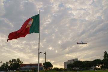 Blowing Portuguese flag on Square of Spain in Lisbon, looks like airport area, the aircraft taking off or landing nearby