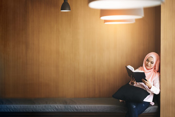 Beautiful young muslim woman reading a book in front of wooden wall with copy space.