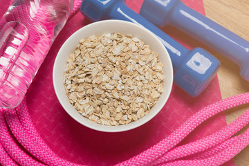 pink fitness mat or for yoga on the floor, dumbbell on the mat, gymnastic skipping rope, muesli and a bottle of water, concept of sports nutrition and healthy lifestyle, close-up of shooting
