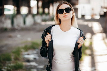 Girl wearing t-shirt and leather jacket posing against street , urban clothing style. Street...