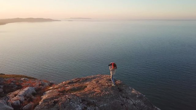 aerial footage of female photographer taking pictures on the cliff during sunset