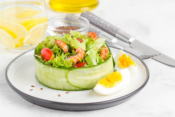 Fresh salad with crayfish necks, lettuce, cherry tomatoes, egg in a ring of cucumbers