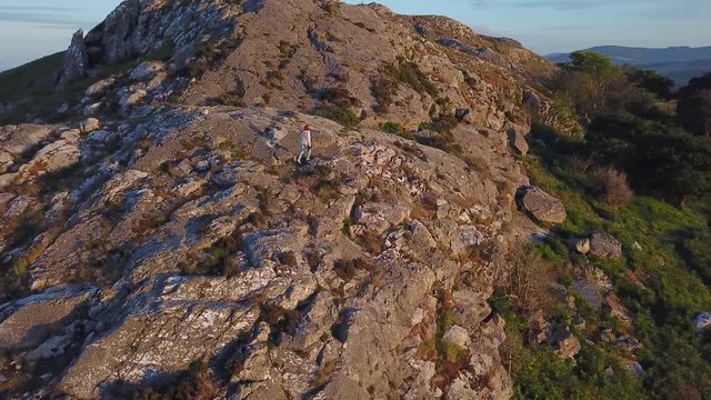 aerial footage of female photographer taking pictures on the cliff during sunset