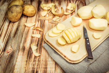 Obraz na płótnie Canvas Raw peeled sliced potato, pile of potatoes and knife on rustic wooden table.