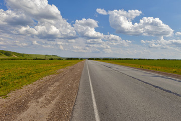 Fototapeta premium Road in the field, long distance trail in the field. Beautiful green hills. Blue sky with fluffy clouds