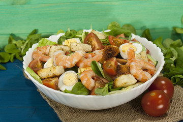 Shrimp salad with salad, arugula, quail eggs, cherry tomatoes, olive oil and balsamic vinegar on a wooden table. Caesar salad with shrimp.