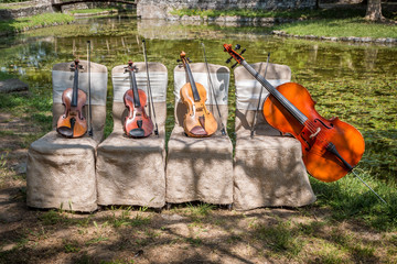 Music and nature concept. String instruments, one cello and three violins on the ceremonial chairs in nature.