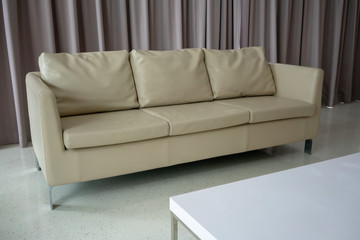 New white leather couch on white floor against light brown curtain.