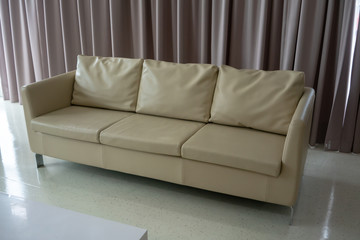New white leather couch on white floor against light brown curtain.