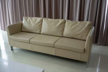 New white leather couch on white floor against light brown curtain.