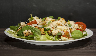 Healthy green organic Caesar salad with cheese, chicken, cherry tomatoes and croutons on a wooden table.