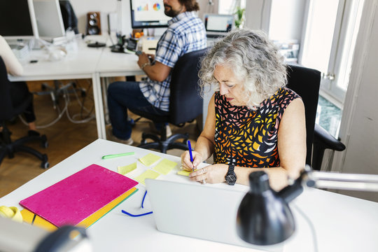 Female editor writing on adhesive note