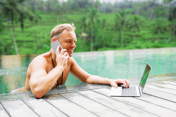 Man using laptop and speaking on phone by the pool © Kaspars Grinvalds