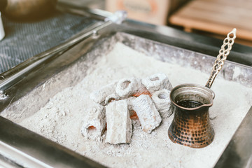 Preparation of Turkish coffee in the cezve in the sand at cafe bar