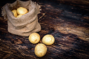 Raw potatoes in a linen bag on dark wooden background with copy space.