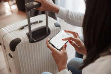 Cropped photo from top of couple with luggage at hotel room, brunette woman holding smartphone and checking location using map. Holiday or vacation concept
