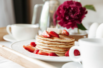 Closeup photo of breakfast in bed with white linen. Pancakes, boiled eggs, coffee, orange juice on...