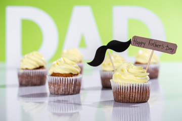creamy cupcakes with mustache sign and Happy fathers day inscription in front of dad inscription made of white letters on green