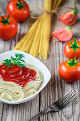 Spaghetti pasta with tomato sauce in plate and tomatoes on wooden table.
