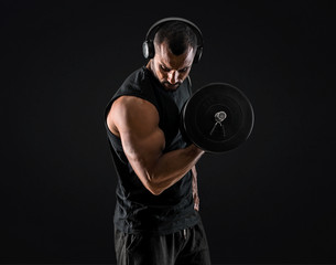Strong handsome sport man making weightlifting, listening music and exercising the biceps on...