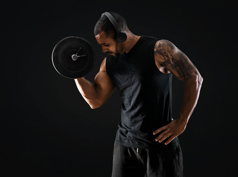 Strong handsome sport man making weightlifting, listening music and exercising the biceps on isolated black background