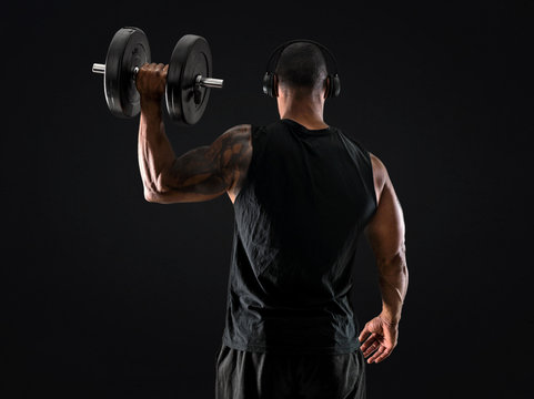 Strong handsome sport man making weightlifting, listening music and  exercising the shoulders on isolated black background