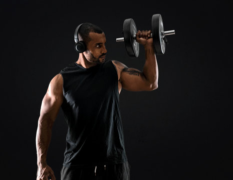 Strong handsome sport man making weightlifting, listening music and  exercising the shoulders on isolated black background