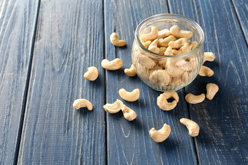 Tasty cashew nuts and glass jar on wooden background
