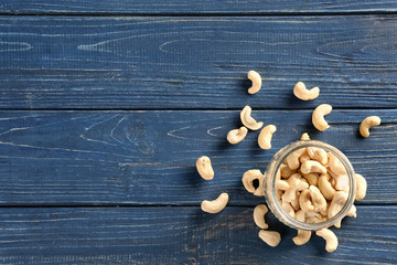 Tasty cashew nuts and glass jar on wooden background, top view