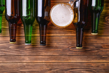 Fresh beer in glass bottles and mug on wooden background