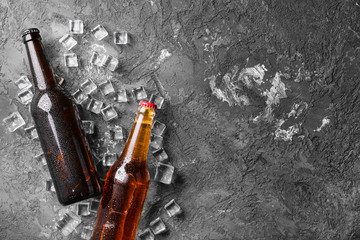 Fresh beer in glass bottles and ice cubes on gray background