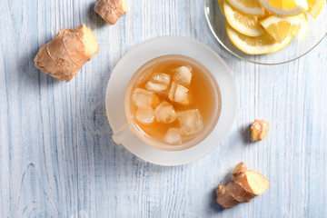 Cup of delicious tea with ice and ginger on wooden table