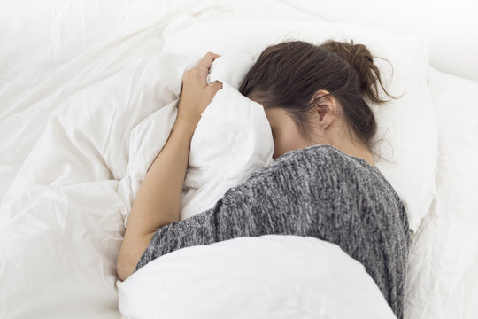 Pensive young woman lying down in bed