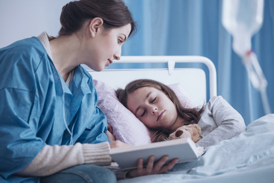 Caregiver reading book to sleepy sick girl in the clinic