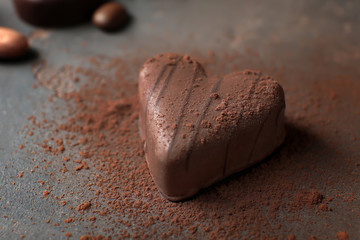 Tasty chocolate candy with cocoa powder on textured table