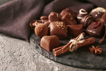 Slate plate with different tasty chocolate candies on textured table