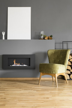 Mockup of white empty poster above fireplace in grey apartment interior with green chair. Real photo