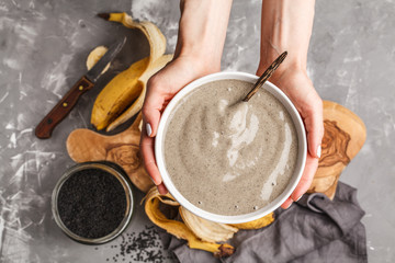 Fototapeta na wymiar Vegan banana and black sesame milk smoothie bowl in hands for healthy breakfast. Healthy vegan food concept.