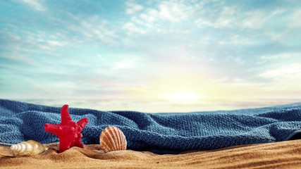 Sea shells and towel on sand and copy space for decoration or products. Cloudy and sunny sky in the...