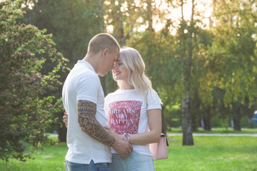 Fototapeta premium Blonde girl with a guy in a park standing among trees hugging each other and looking each other in the eyes
