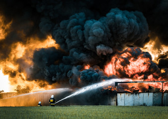 Firefighters spraying water in front of huge fire and black smoke