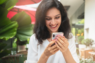 Happy woman with smartphone in a restaurant terrace with an unfocused background